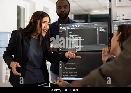 Female manager expresses frustration with employee over incomplete web development project, emphasizing need to meet deadlines. Colleagues share coding updates and work together to resolve tasks. Stock Photo