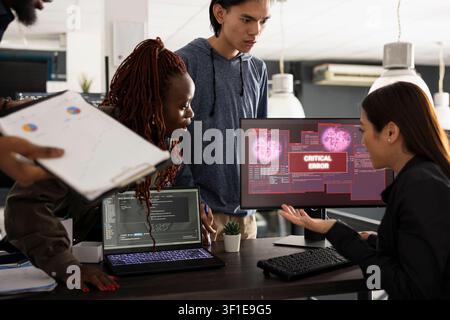 Multiethnic team of developers working anxiously to resolve unexpected critical error on computer. Concerned Asian woman collaborates with colleagues to fix system crash in modern office. Stock Photo