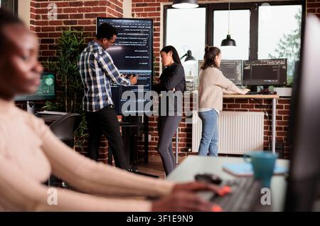 Diverse tech engineers use binary code to program firewall encryption and develop network security software on a shared server system. Stock Photo