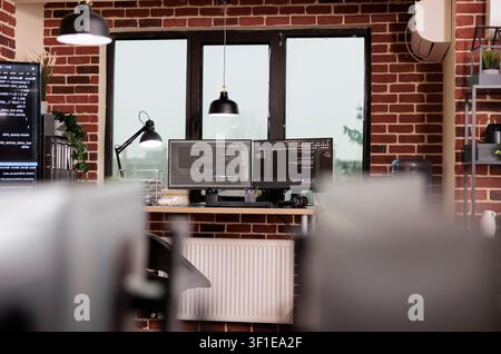 Desk with multiple monitors runs terminal windows and database scripts in an empty programming office focused on cloud computing and system code. Stock Photo