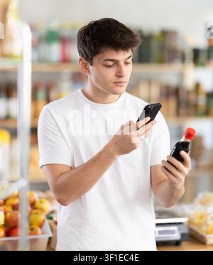 Guy scanning barcode on soy sauce using phone in food store Stock Photo