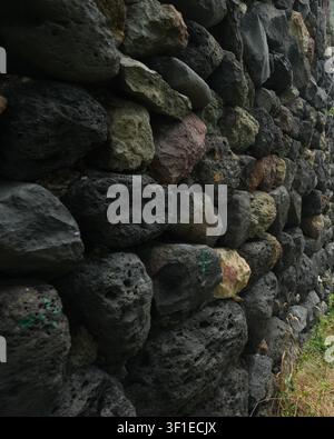 A close-up shot showcases a rustic wall built from textured volcanic stones of various dark shades and sizes Stock Photo