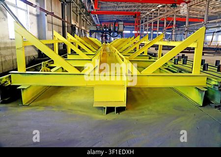 A dramatic, symmetrical wide shot of bright yellow-painted steel structural frames arranged in a repeating V-pattern on an assembly line, set against Stock Photo