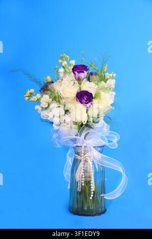 A romantic and elegant bridal bouquet featuring a mix of white lisianthus, delicate filler flowers, and deep purple roses, arranged in a textured glas Stock Photo