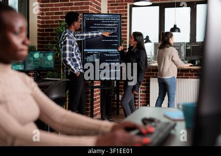 Backend network developer explains application code to a coworker as the team builds security layers for stable software functionality. Stock Photo