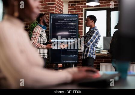 Software developer points out a cloud database algorithm error while discussing corrupted encrypted files and cyber security with a colleague. Stock Photo