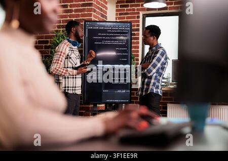 Programming engineers analyzing code on screens with programmers, screens and infrastructure details supporting software development and system monitoring. Stock Photo