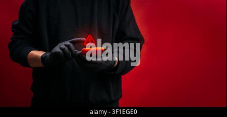 Cybercrime featuring hacker using smartphone with digital warning symbol. Online fraud, phishing attacks, scam messages, identity theft, data breaches Stock Photo