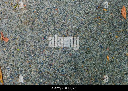 A flat lay, top down close up shot showcasing a rough textured concrete or asphalt ground embedded with small gravel stones, and pebbles. Stock Photo