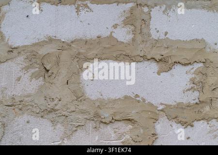 High-resolution closeup showing weathered exterior wall with rough plaster, exposed aggregate, irregular repair patches, beige and off-white tones, gr Stock Photo