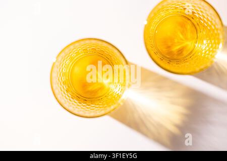 Empty amber drinking glasses casting golden shadows on white background Stock Photo