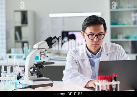 Asian Male Scientist Analyzing Data on Laptop in Medical Laboratory Stock Photo