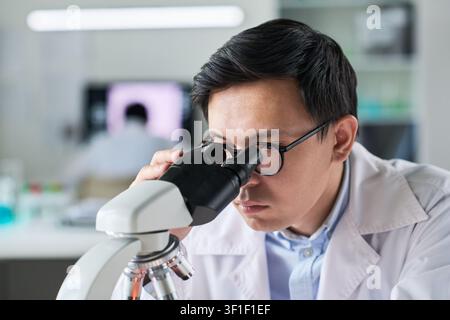 Asian Scientist Examining Samples through Microscope in Lab Stock Photo