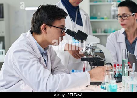 Asian Male Scientist Using Microscope during Team Lab Testing Stock Photo