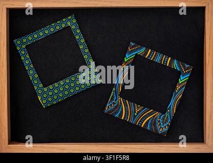 Two handmade instant photo style frames decorated with colorful African patterned Shweshwe fabric and arranged on a black chalkboard within a wooden f Stock Photo