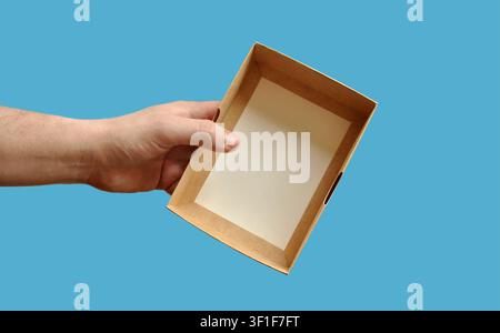 Brown box in hand, blue background. Blank, empty cardboard box. Sustainable packaging concept, packaging template, sales, warehouse, paper industry Stock Photo