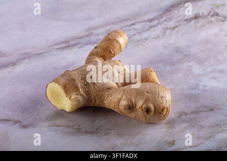 Fresh ginger root displayed on light marble background. Natural lighting highlights texture pale yellow interior. Composition focuses on organic shape Stock Photo