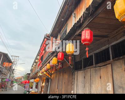 Antique red and yellow Chinese lanterns hang on old wooden buildings along the street. Stock Photo