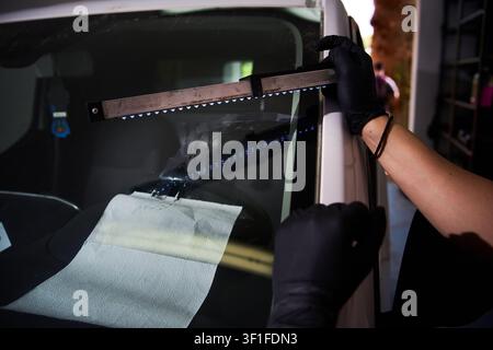 Windshield UV Resin Curing. Windshield repair. Automotive technician holds ultraviolet lamp over broken car glass. Mechanic cures resin inside windshi Stock Photo