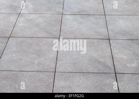 A close-up view of a paved surface composed of square grey tiles with visible texture and grout lines creating a repeating pattern Stock Photo