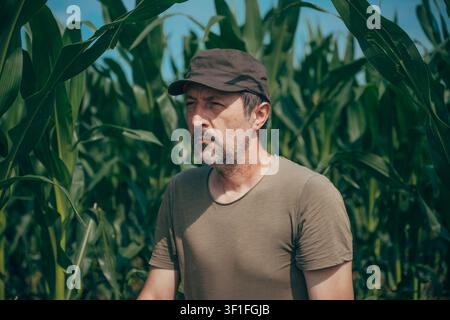 Portrait of a farmer standing in a green cornfield during the growing season. Agriculture, crop production, rural life and farming concept. Selective Stock Photo