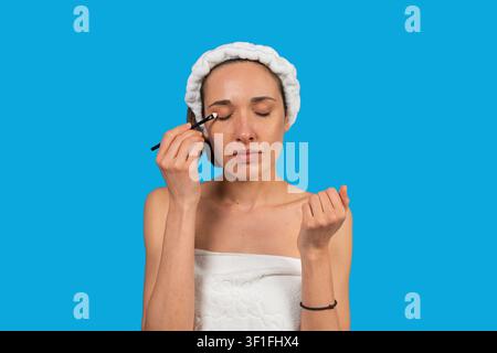 Woman in towel wearing headband applying eyeshadow on closed eyes Stock Photo