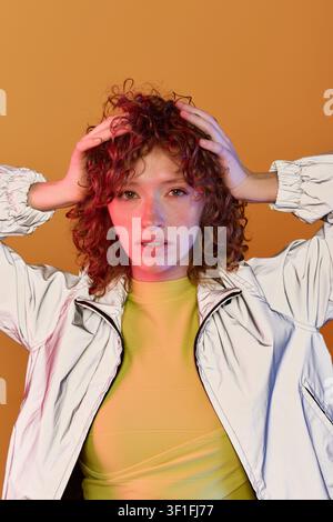 A stunning young woman with red curls showcases effortless style in a chic outfit. Stock Photo