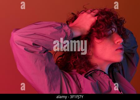 A young woman with stunning red curls poses confidently against a colorful backdrop. Stock Photo