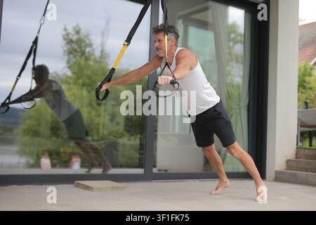 Fit mature man doing suspension training on a patio Stock Photo
