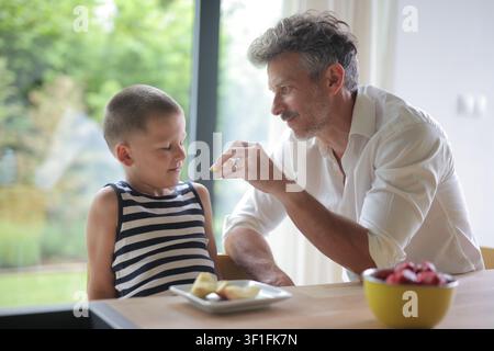 Caring father feeds his son an apple slice Stock Photo