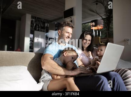 Happy family of four using laptop computer on sofa Stock Photo