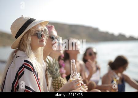 Young woman in a sun hat enjoying a beer with friends Stock Photo