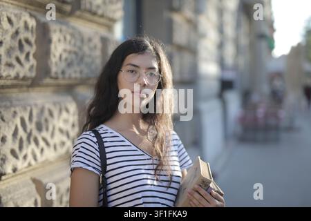 Thoughtful female student holding a book outdoors Stock Photo