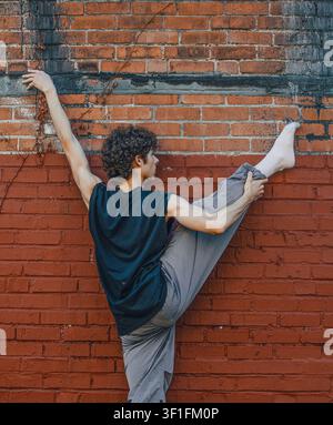 Male dancer holds a standing split against a brick wall Stock Photo