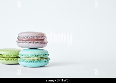 Stack of three colorful French Macarons, cakes with different flavors stacked in a pyramid, mint, apple, currant flavor. macaroons aquamarine, green, purple color on gray background, side view Stock Photo