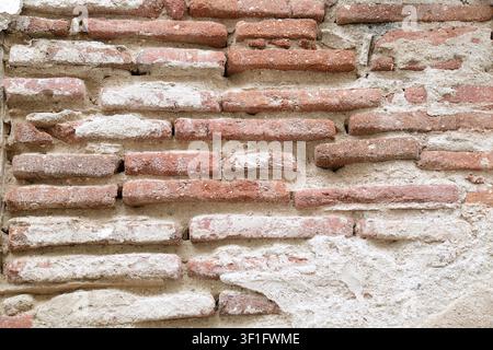 Close-up texture of an ancient weathered red brick wall with remaining white plaster and coarse mortar in the historic town of Elvas, Alentejo region, Stock Photo