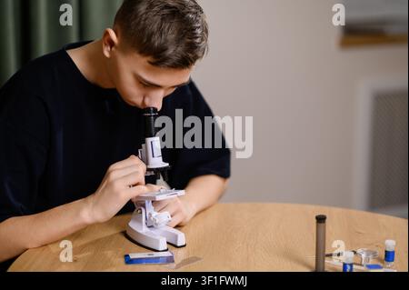 Close up of high school student using optical microscope for biology, exam prep and scientific academic research. Teen boy clever scientist with scien Stock Photo