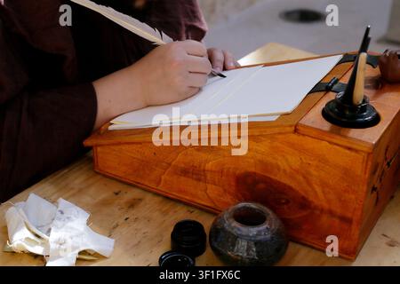 Person writing with a quill on parchment sheets at a traditional wooden writing desk. Stock Photo