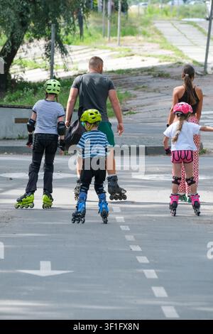 KYIV, UKRAINE, July 11, 2026, Parents and children wearing inline skates and protective helmets skate together on a dedicated park roadway during a su Stock Photo