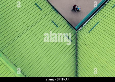 Aerial view of a person walking on a paved area adjacent to a bright green corrugated metal roof in Belgrade, City of Belgrade, Serbia. Stock Photo