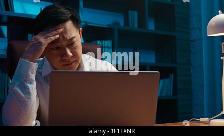 Stressed Asian Korean business man working hard with internet cyberspace laptop difficulties at evening indoors. Frustrated Japanese male Chinese Stock Photo