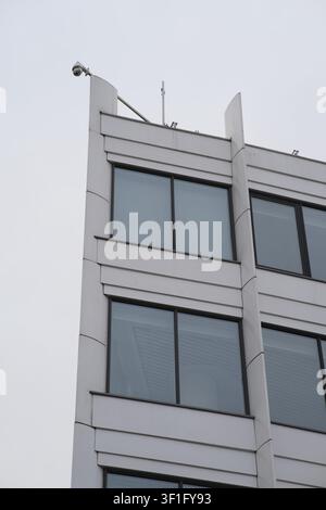 Modern office building with CCTV security camera on the roof corner. Urban architecture detail under overcast sky. Stock Photo
