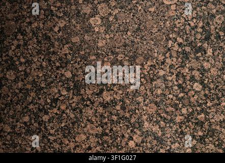 Reddish brown splotchy granite surface with black blotches, crater‑like round patches, gray splotches, lighter streaks and polished shine Stock Photo
