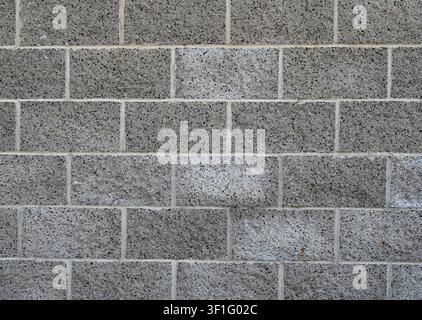 Concrete cinder block wall with decorative exposed dark aggregate, porous cracked mortar, and white mineral deposits on the surface Stock Photo