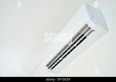 Wall mounted air conditioner operates indoors with open vents and digital temperature display. Cooling system installed on a white wall Stock Photo