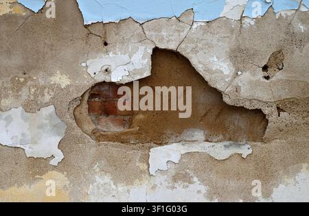 Multilayer wall with cracked painted concrete, exposed terra cotta clay, and a large hole revealing red brick and mortar Stock Photo