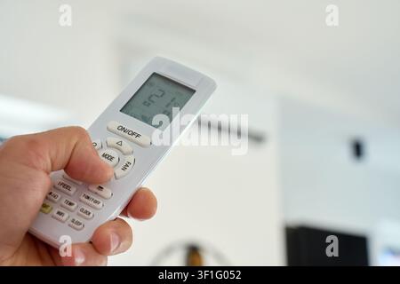Person using air conditioner at home, holding remote control and adjusting temperature at home. Concept of room cooling, temperature control and summer comfort Stock Photo