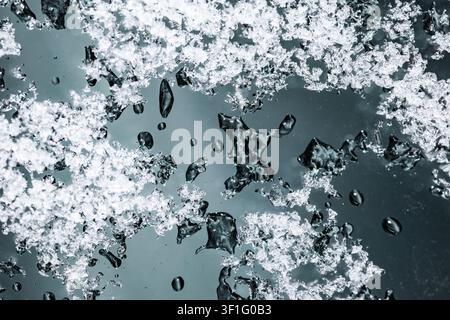 Close up of melting snow crystals and water droplets on a dark glass window pane surface Stock Photo