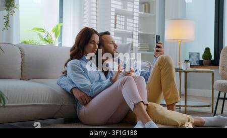 Concentrated gadget addicted Caucasian using gadgets mobile phones apps scrolling at home family man and woman focused browsing devices social media Stock Photo
