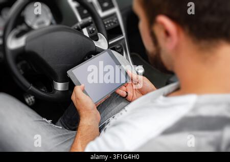 A man sits in the driver's seat of a car and looking at a digital tablet. Stock Photo